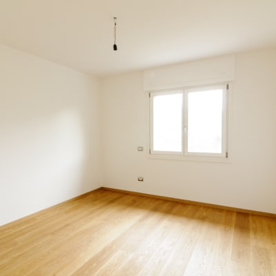 Ett tomt rum med fönster, vita väggar och parkettgolv.