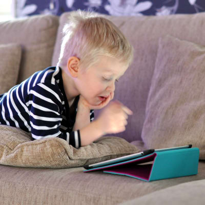 Ett barn ligger på en soffa och tittar på en pekplatta.