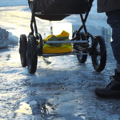 En person skuffar fram en barnvagn på en isig väg.