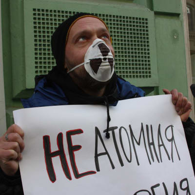 En man i munskydd håller ett ryskspråkigt plakat.