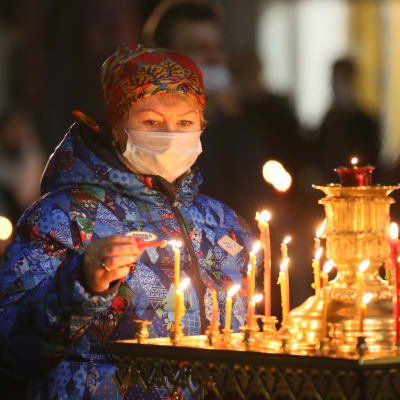 En kvinna i munskydd tänder ljus i kyrka under påsk.