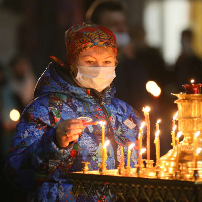 En kvinna i munskydd tänder ljus i kyrka under påsk.