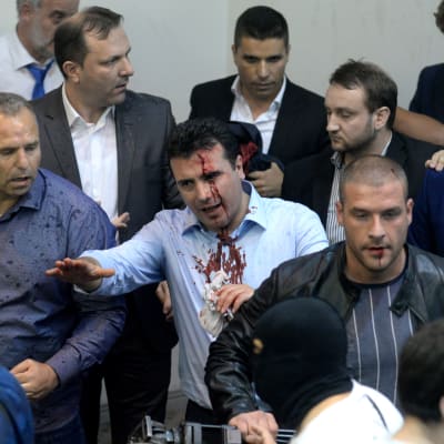 Flera män, en del av dem blodiga, samlade på ett ställe. I mitten står socialdemokratiske ledare i Makedonien Zoran Zaev som blöder från pannan. Han skjorta är också blodig.