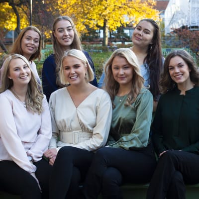 Luciakandidaterna 2019 sitter och står kring en parkbänk. Luciakandidaterna 2019. Från vänster sittande: Julia Wik, Felicia Holländer, Melissa SUndblad, Nea Lundström, Moa Björklund, Sara Ray, Jessica Lindholm. Uppe Minette Bäckblom, Wilma Rehnst