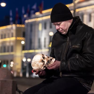 Lukupiirin toimittaja Jukka Kuosmanen istuu Helsingin keskustassa Keisarinnan kivellä Kauppatorilla aikaisin aamupimeydessä pääkallo käsissään 