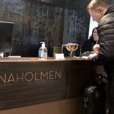 Manlig hotellgäst skriver in sig på Hanaholmen, handsprit i flaska på disken