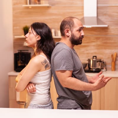En kvinna och en man står rygg mot rygg i ett kök. 