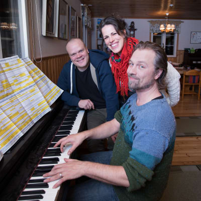 Tre personer vid ett piano