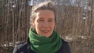 Tjänsteman på Migri i halsduk står ute bredvid en björkdunge
