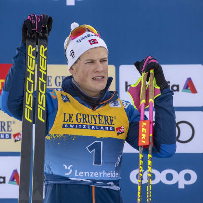 Johannes Hösflot Kläbo står med skidorna höger hand och stavarna i vänster.