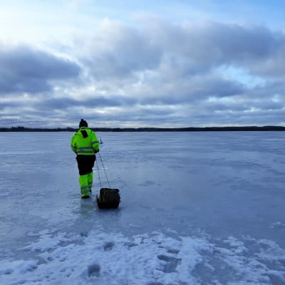 Kalastaja vetää ahkiota järven jäällä.