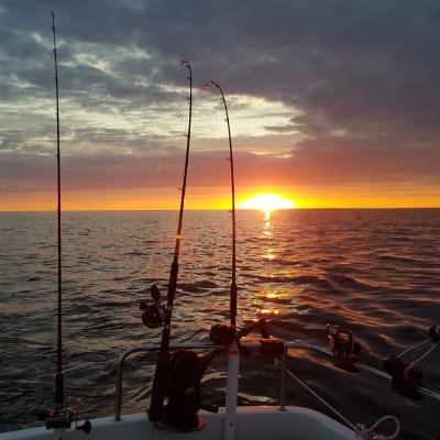 Solnedgång vid havet. På bilden syns en båt och tre metspön.