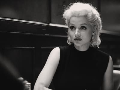 Svartvit bild på Marilyn Monroe (Ana de Armas) då hon sitter vid ett bord och ser osäker ut.