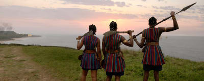 Nawi (Thuso Mbedu), Nanisca) Viola Davis och Amenza (Sheila Atim) står med ryggen mot kameran på en höjd vid kusten och ser ut över havet och en soluppgång. 
