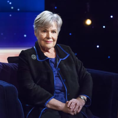 Elisabeth Rehn sitter i en blå sammetsfåtölj hos Daniel Olin. 