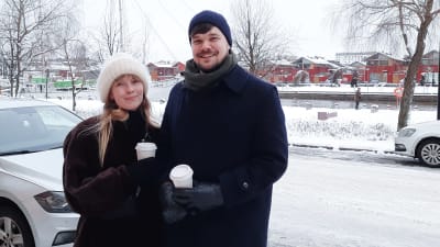 En ung Kvinna och en man står på Ågatan i Borgå. Det är snö på marken och de håller i var sin take away-mugg.