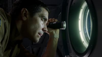 David (Jake Gyllenhaal) blinkar med ficklampa ut genom fönstret på rymdstationen.