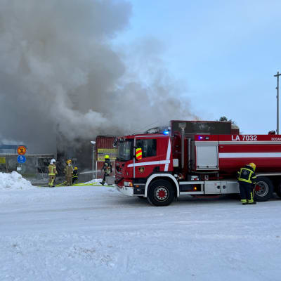 Saariselän palanut kauppakeskus Kuukkeli savuaa. Paloauto ja palomiehet ovat sammutustöissä.