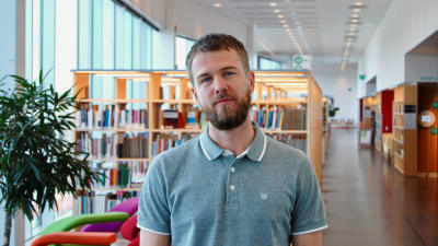 Robin Ekelund, en vit man med skägg, står i ett bibliotek.