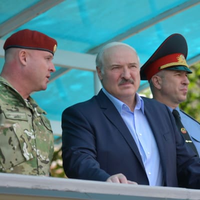 Belarus president Aleksandr Lukasjenko står mellan två militärer och lyssnar på den ena som talar.