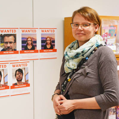 En kvinna står framför en vägg med bilder på misstänkta personer.