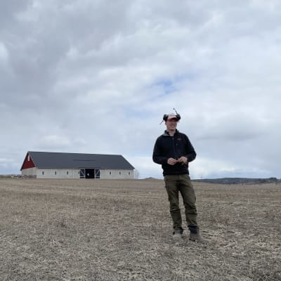 Maanviljelijä Erik Perklen seisoo keskellä karua peltoaan Siuntiossa kuulokkeet päässään.