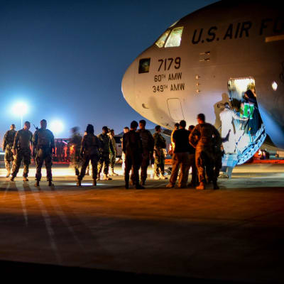 Upplyst flygplats där människor kliver ut ur ett flygplan på väg till väntande bussar. Evakuerade afghaner landar i Kuwait den 24 augusti.