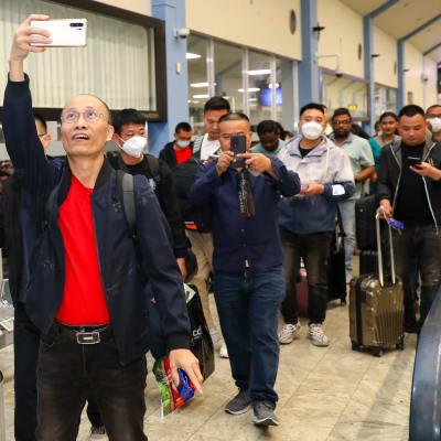 Kiinalaisia turisteja kävelee lentokentällä. Osa heistä ottaa kuvia.