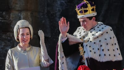 Drottning Elizabeth (Olivia Colman) och prins Charles (Josh O'Connor) vinkar på en balkong, bilden är tagen under inspelningen av serien The Crown.