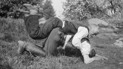 Två män leker "ryggbördan", där den ena ligger på den andras rygg, Den undre ska försöka stiga upp, den andra ska hindra honom att göra det. Bilden är tagen 1929 i Strömfors, Kungsböle.