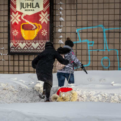 Två kvinnor klättrar över en snövall vid övergångsstället