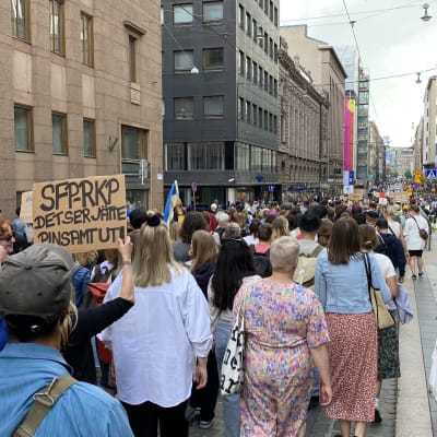 Demonstranter går längs med Alexandersgatan i Helsingfors. En bär en skylt med texten "SFP RKP det ser jätte pinsamt ut!"