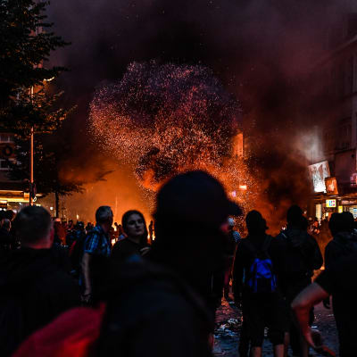 G20-demonstranter vid området Schanzenviertel i Hamburg står vid brinnande barrikader med ett stort rökmoln som stiger upp i luften.