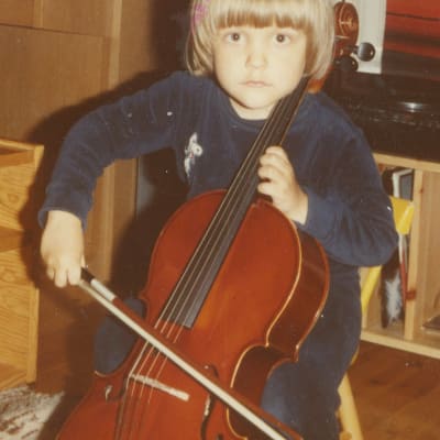 Noin kolmivuotias poika soittaa selloa kotona. Taustalla ryijy, piano ja levysoitin, lattialla räsymatto.
