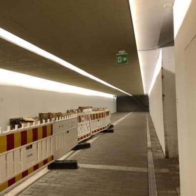 En tunnel med vita väggar och asfalterat golv. Tillfälliga staket till vänster.