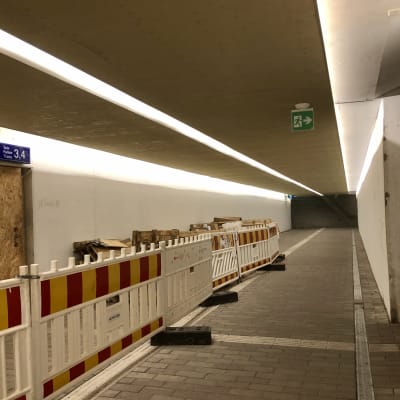 En tunnel med vita väggar och asfalterat golv. Tillfälliga staket till vänster.