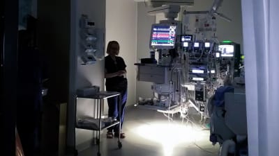 Ett rum i en sjukhus, det är mörkt, medicinsk utrustning med många skärmar lyser i bakgrunden. Man ser en siluett av en sköterska.