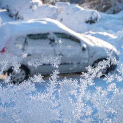 En snötäckt personbil fotograferad genom ett fönster med rimfrost.
