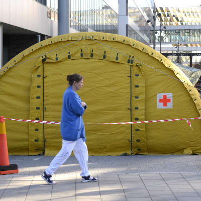 Ett gult tält utanför Karolinska universitetssjukhuset och en sjukskötare som går förbi. 
