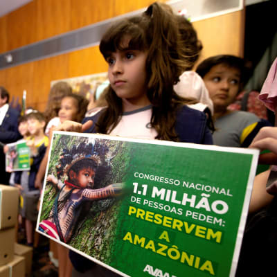En liten flicka står med en skylt för att rädda Amazonas. 