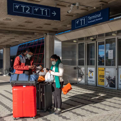 Helsinki-Vantaan lentoasemalla, Terminaali 1 edustalla, kaksi matkustajaa kasvosuojukset päällä.