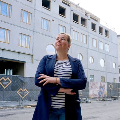 Kvinna i blå jacka står framför ett bygge.