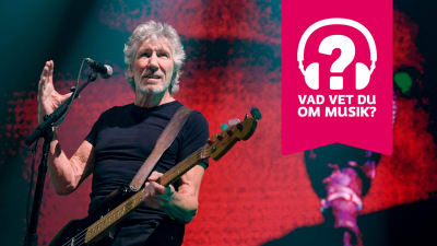 Roger Waters har en elbas kring halsen, står bakom en mikrofonställning och håller upp höger hand en aning.