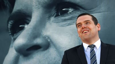 Konservativa partiets ledare i Skottland Douglas Ross med en plansch på Nicola Sturgeon i bakgrunden