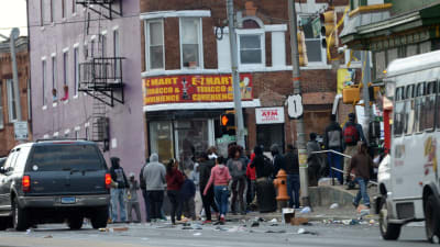 En grupp människor utanför en butik i Baltimore. Skräp ligger på gatan.