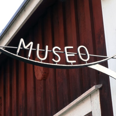 Metallinen museo kyltti punaisen puutalon seinässä.