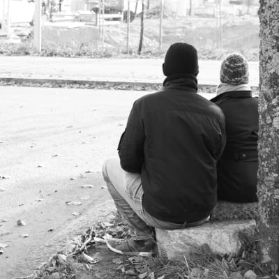 två personer sitter på gatstenar, svartvit bild