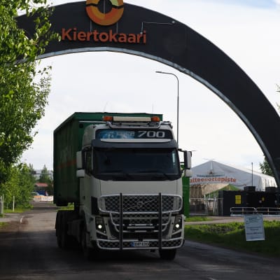 Jätteenkuljetusauto poistuu kaarevan portina alla jätekeskuksesta. Vasemmalla koivuja.