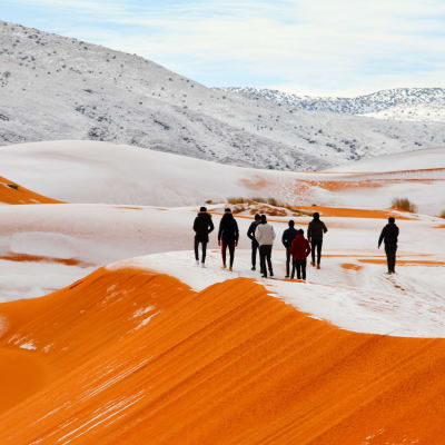 Människor vandrar på snötäckta sanddyner.