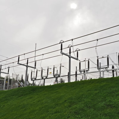 Sähkönjakeluasema ja sähköjohtoja ja sähkölinjoja vihreän nurmikon peittämällä mäellä.